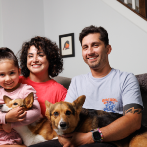 Man and woman sitting on couch with young girl and two dogs on their laps.
