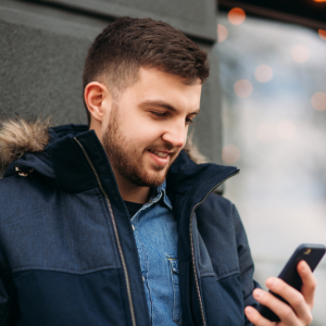 Young man in parka standing outside looking at his cell phone